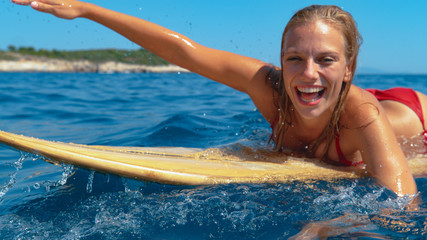 PORTRAIT: Smiling surfer girl having fun swimming to the line up to catch waves.