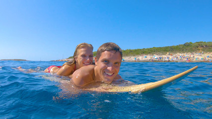 PORTRAIT: Tourist couple enjoys lying on a surfboard and paddling around sea