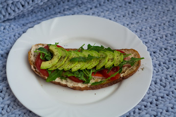 Toast of dark bread, avocado with tomato and arugula. Healthy food, breakfast of fresh vegetables.