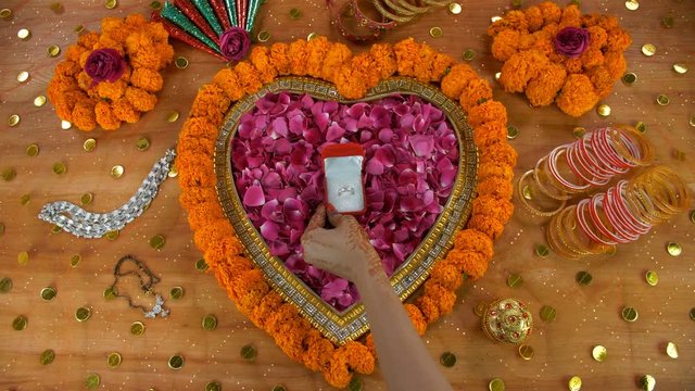 Closeup of mehndi on woman hands placing the red box of her engagement ring. Top view of the beautiful diamond ring surrounded by wedding items like Payal  mangal sutra  sindoor  mehndi cones  and ...