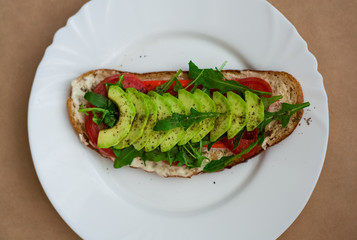 Toast of dark bread, avocado with tomato and arugula. Healthy food, breakfast of fresh vegetables.