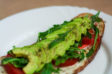 Toast of dark bread, avocado with tomato and arugula. Healthy food, breakfast of fresh vegetables.