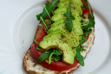 Toast of dark bread, avocado with tomato and arugula. Healthy food, breakfast of fresh vegetables.