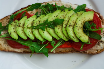 Toast of dark bread, avocado with tomato and arugula. Healthy food, breakfast of fresh vegetables.
