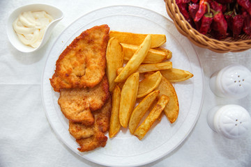 Fried chicken cutlet. Fry the potatoes in a white plate . Red Dry Pepper in Traditional Basket . Mayonnaise inside a bowl .