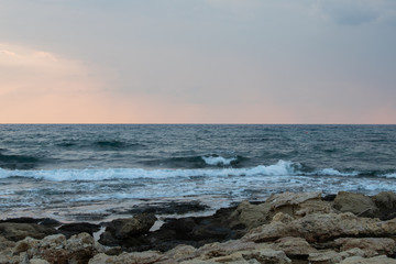 rocky sea coast at sunset, waves breaking on the rocks, small pools formed by nature in the rocks with a reflection of the dark sunset sky before a thunderstorm
