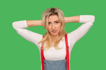 Don't want to hear! Portrait of irritated adult woman in denim overalls covering ears, avoiding...