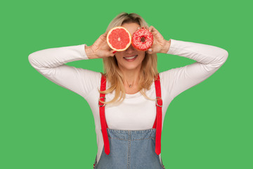 Healthy fruits vs junk food. Portrait of playful stylish woman covering eyes with doughnut and...