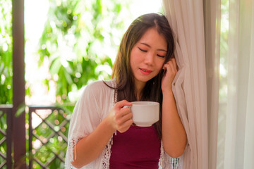 lifestyle portrait of young happy and beautiful Asian Japanese woman having morning coffee or tea at hotel terrace or home balcony smiling relaxed and cheerful