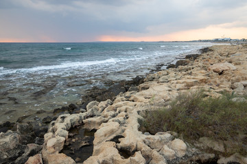 rocky sea coast at sunset, waves breaking on the rocks, small pools formed by nature in the rocks with a reflection of the dark sunset sky before a thunderstorm