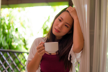 lifestyle portrait of young happy and beautiful Asian Korean woman having morning coffee or tea at hotel terrace or home balcony smiling relaxed and cheerful