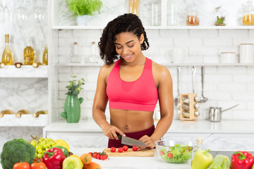 Beautiful young afro woman preparing vegetable salad at home