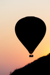 One hot air balloon floating over hills into an orange sunset