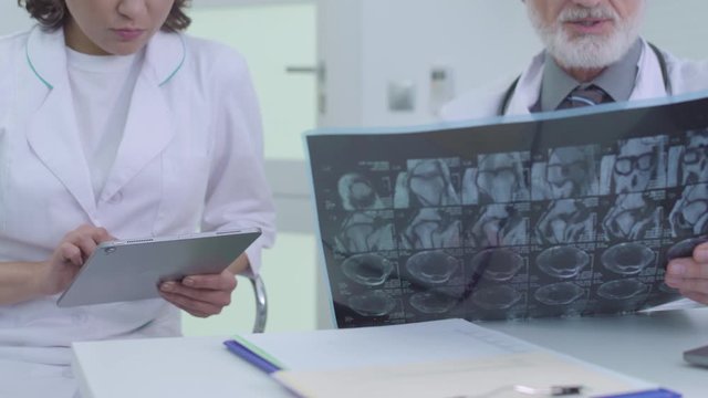 Nurse typing on tablet, listening to senior doctor, analyzing tomographic image