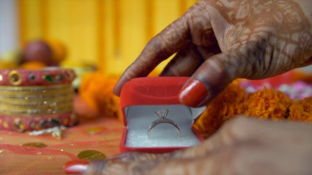 Closeup shot of mehndi on woman hands showing her beautiful wedding ring. Indian bride's engagement ring in a small red box placed on a decorated floral platform - wedding jewelry concept