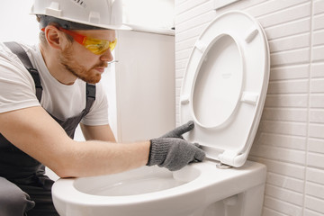 Plumber installing toilet bowl in restroom, work in bathroom