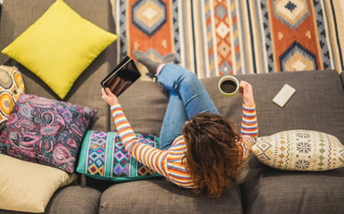 Obraz premium Top view of young woman watching videos on tablet while drinking coffee at home during isolation quarantine - Tech, stylish and lifestyle trends concept - Focus on female head