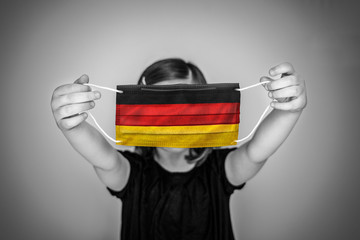 A child girl show a protective medical mask against bacteria and viruses with the flag of Germany.