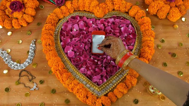 Closeup of mehndi on woman hands placing her wedding ring in a small red box. Beautiful engagement ring placed on a decorated platform surrounded by mangal sutra  Payal  and traditional sindoor