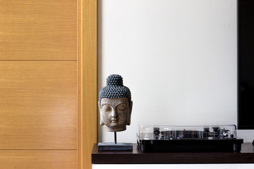 Corner of stylish house, with Buddha head, record player on white cabinet.