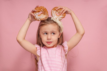 Cute little girl having fun with donuts on ears isolated on a pink background. Happy childhood with a delicious dessert.