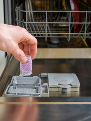 Loading the soluble-coated tablets in the dishwasher. Powder, dishwashing detergent and rinse aid. Washing dishes in the kitchen.