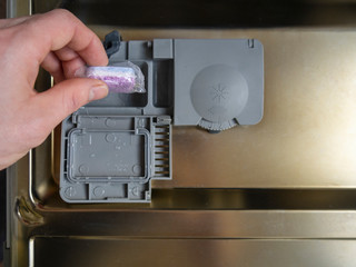 Loading the soluble-coated tablets in the dishwasher. Powder, dishwashing detergent and rinse aid. Washing dishes in the kitchen.