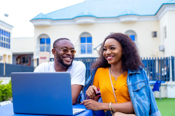 young black man and a beautiful woman sitting out, discussing and working casually on a laptop