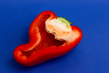 Half a juicy red bell pepper. Healthy and veggie nutrition. Bright blue background. Close-up.