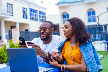 young black man and a beautiful woman sitting out, discussing and working casually on a laptop