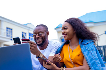 young black man and a beautiful woman sitting out, discussing and working casually on a laptop