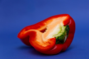 Half a juicy red bell pepper. Healthy and veggie nutrition. Bright blue background. Close-up.