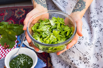 Green lettuce leaves salad with sesame seeds dressing. Vegan food. Woman hands.