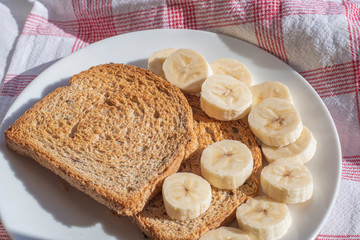 Toasted slices of bread with banana slices on a plate under a bright summer saline