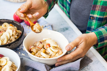 Oatmeal granola porridge with apple and banana fruits and nuts. Vegan healthy sweet breakfast. Woman hands