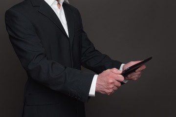 Businessman in black suit holding tablet pc in his hands closeup side view. Two hands holding device