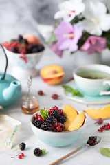 Granola or muesli with berries and fruits for a healthy breakfast in the morning with a bouquet of summer flowers on a light table.