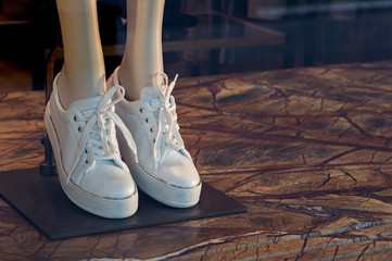 Women's white sneakers with a shiny inset along the contour on the legs of a mannequin in a shop window. Background