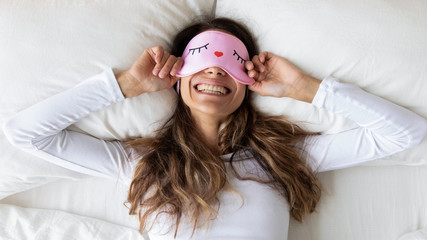 Top view close up happy woman wearing funny sleeping mask enjoying morning in bedroom, lying in...