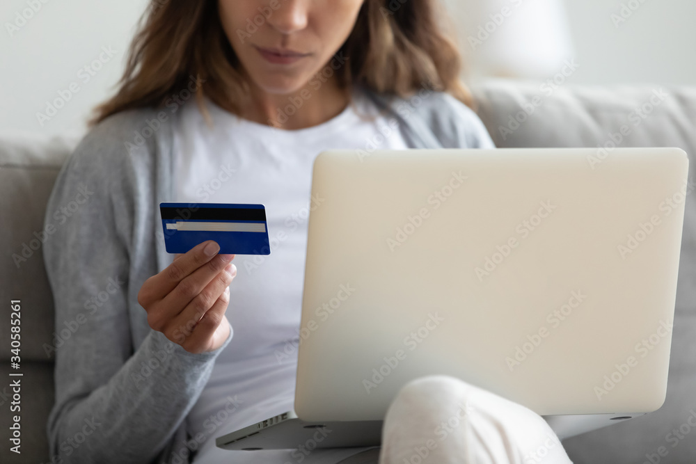 Wall mural close up woman holding credit card and using laptop, sitting on sofa at home, young female customer 