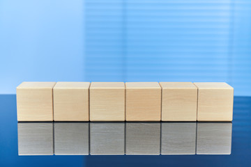 Six wooden cubes on a blue background in a row with a reflection on the surface. Free space for letters, numbers, symbols, or labels. Layout for infographics.