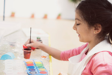 Little girl paints with tempera paints in her backyard
