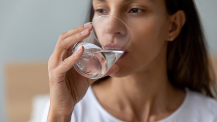 Close up thirsty beautiful young woman drinking pure water from glass, holding in hand, dehydrated attractive girl enjoying clean mineral water, healthy lifestyle concept, natural beauty