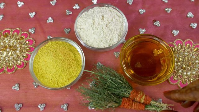 Closeup of woman hands placing bunches of Durva grass on a decorated platform. Top view of a decorated surface with glass bowls of Haldi powder  mustard oil  flour  and Durva grass - Haldi ceremony