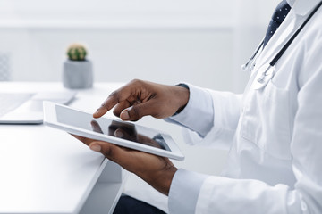 Cropped of black doctor using digital tablet at workplace