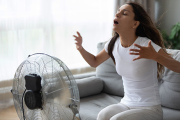 Overheated woman enjoying fresh air, cooling herself by electric fan close up, exhausted tired...