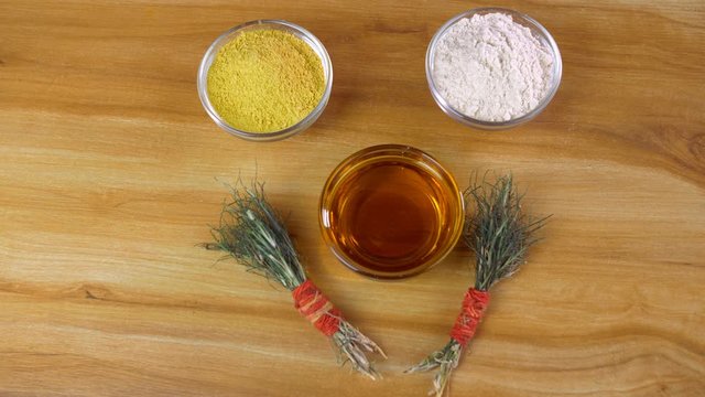 Pan shot of beautifully placed Haldi ceremony items placed on a wooden table. Closeup shot of glass bowls with Haldi powder  mustard oil (Sarson ka tel)  flour  and bunches of Durva grass 