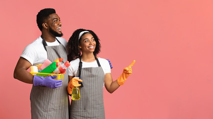 Smiling couple holding basket with detergents and pointing at copy space