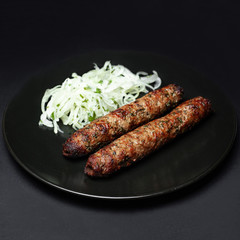 lula kebab with salad on a black plate on a black background.