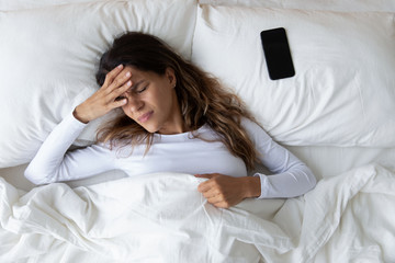 Top view unhappy woman feeling headache after sudden awakening by phone call, message signal or...